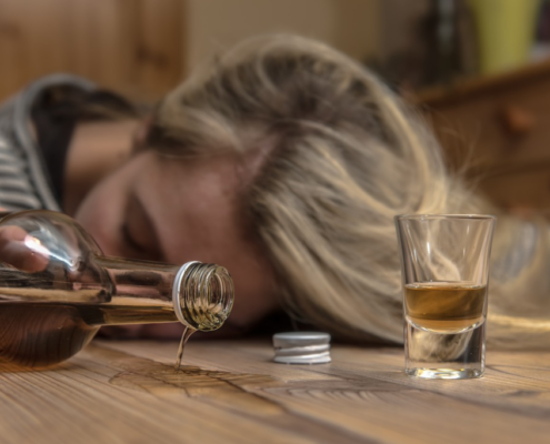 A person lying unconscious on the floor beside an empty bottle, illustrating the dangers of alcohol poisoning