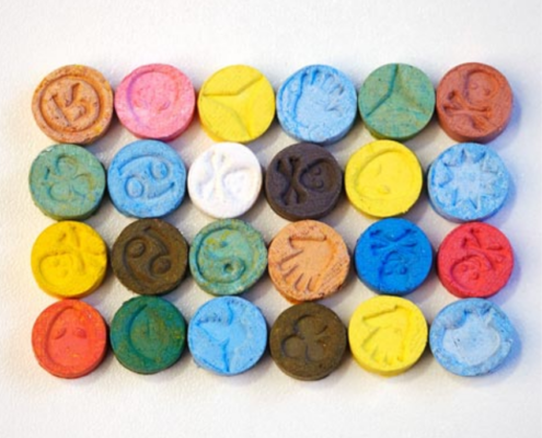 A variety of colorful MDMA (Molly) tablets arranged on a white surface, representing the different forms in which the drug is consumed.