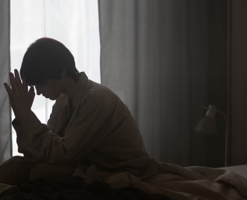 A lesbian in their bed, looking anxious and depressed.