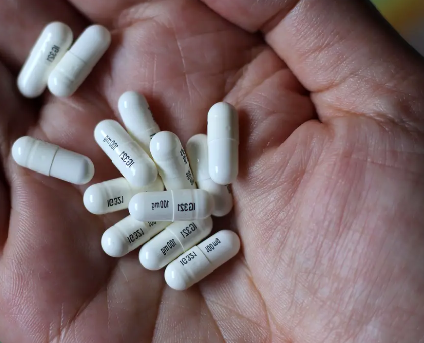 A hand with white gabapentin capsules.