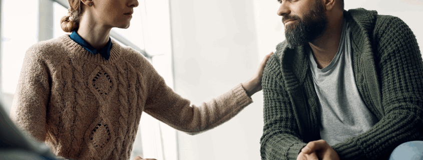 A female therapist comforting a gay person in a trauma-informed addiction treatment center.